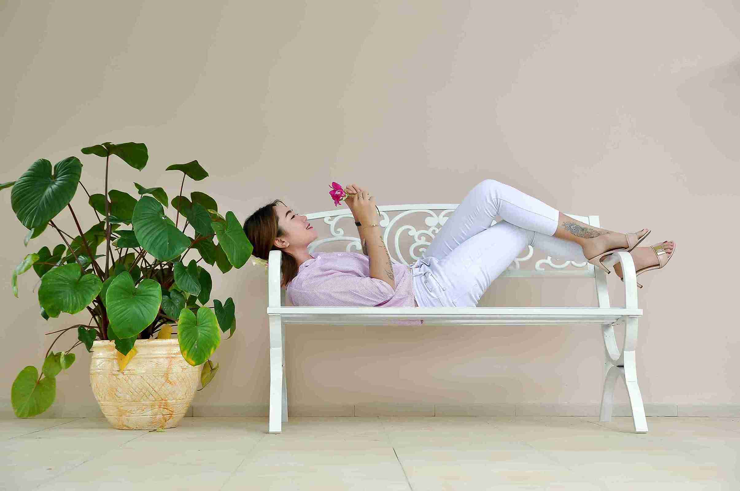 girl laying on a bench near green plant with a flower in hand