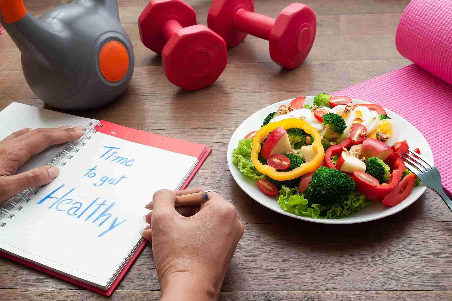 dumbbells and a wommen writing a diary of her healthy habits